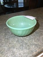 Photo of single vintage jadeite green glass mixing bowl showing top view and interior, placed on countertop.
