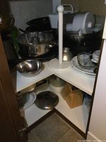 Corner cupboard shelf with stainless steel mixing bowls, a bundt pan, plastic storage containers, a metal pot, and a paper towel holder