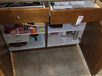 Lower kitchen cabinet drawers and shelves with various kitchen items including bakeware, glassware, and storage containers