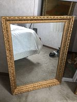 Front view of large rectangular mirror with gold leaf frame reflecting a bedroom scene.