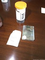 Clear photo of a container, a transparent coin case with old coins inside, and a white piece of paper on a brown surface.