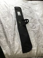 Black soft-sided pool cue carry case lying flat on a light-colored patterned fabric surface.