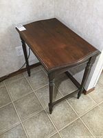 Front side view of vintage wooden side table showing turned legs and rectangular tabletop with curved edge detail.