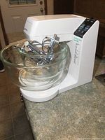 White Black & Decker stand mixer with two clear glass bowls and metal attachments placed inside bowls.