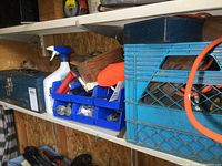 Shelf containing blue metal toolbox labeled 'Drill', small plastic organizer bins with assorted hardware, and a blue milk crate with miscellaneous items including an orange extension cord.