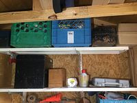 Shelf with plastic milk crates, black metal toolbox, wooden box, gray plastic toolbox and small containers, showing tool storage and contents.