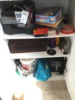 Shelf with various tool cases, Rummikub game box, battery packs, red tape measure, blue tool bag and other small tool-related items.