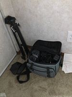Overview of black metal tripod and gray soft camera bag with internal accessories