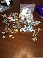 Photo of assorted vintage costume jewelry laid on wooden table, including necklaces, brooches, and a sealed bag with pearl bead necklaces.