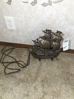 Full view of the vintage cast metal ship lamp placed on carpet near a wall outlet, showing the electrical cord.