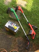 Two electric weed trimmers and Radley leaf blower box on grass and stone path
