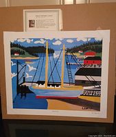 Full view of the lithograph depicting a ship at dock with surrounding landscape by Maud Lewis mounted on brown backing board.