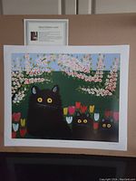 Image of an unframed offset plate lithograph print by Maud Lewis showing three black cats with yellow eyes in a floral setting, mounted on cardboard backing.