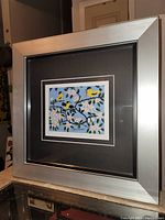 Front and side view of the framed fine art print; showing silver modern frame and black double mat with artwork inside.