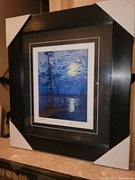 Framed fine art print by Tom Thomson titled 'Moonlight' shown from an angle, with black frame and white corner protectors.