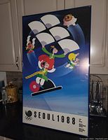 Framed 1988 Seoul Olympic poster with stylized cartoon athletes and mascot on blue background, showing full poster vertically.