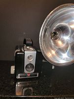 Front side view showing the camera body, lens, viewfinder, and flash attachment.