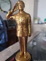 Front view of gold finished metal World War II soldier statue saluting, showing detailed uniform and facial features.