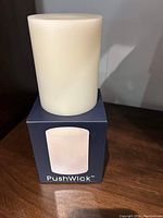 Ivory-colored battery operated candle sitting on top of its original blue box with PushWick branding.