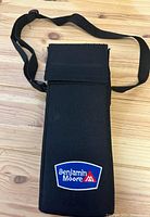 Black Benjamin Moore branded fabric carrying case with a flap closure and adjustable shoulder strap, placed on a wooden surface.