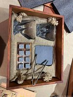 Wooden tray with whiskey glass, six stone chilling cubes, metal tongs, and coasters inside a burlap lining.