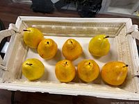 Top view of nine yellow decorative pears placed inside a white rustic-style tray with rope handles.