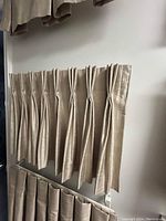 Beige pleated drapery panels displayed on wall for staging.
