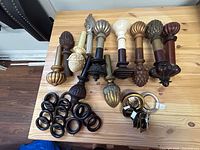 Eight decorative drapery finials and a cluster of several black wooden curtain rings on a wooden surface.