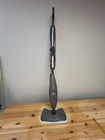 Full view of the upright Shark steam mop floor cleaner on a wooden surface against a plain wall.