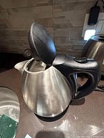 Electric kettle with open lid showing stainless steel interior and black handle, sitting on kitchen counter.