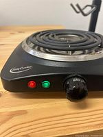 Front and side angled view of Betty Crocker electric hot plate burner showing the heating coil, control knob, and indicator lights on wooden surface.