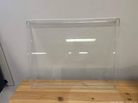 Clear acrylic tray placed vertically against a white wall showing full rectangular frame and transparency.