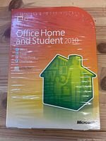 Sealed box showing front cover with Microsoft Office Home and Student 2010 branding and list of included programs: Word, Excel, PowerPoint, OneNote