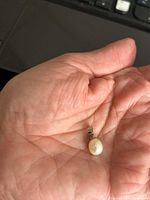 Pearl pendant held in hand to show size and detail, showing off-white teardrop-shaped pearl with silver bail.