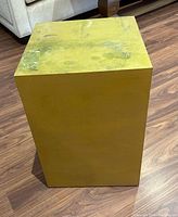 Front angle view of the yellow square pedestal stand showing its height and worn paint finish.
