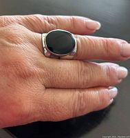 Ring worn on finger showing black onyx stone and silver band.