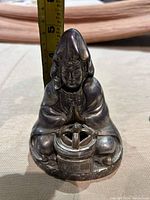 Front view of the metal incense burner holder resembling a seated figure with hands in prayer, holding the incense burner.