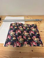 Silver roll of clear wrapping paper on table next to white and floral tissue paper sheets.