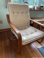 Angled front-left view of the chair showing the curved oak armrest and side frame and the textured upholstered tufted cushion seat and back.