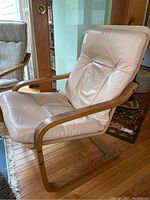 Front and side view of light pink leather armchair with curved wooden frame and arms, showing upholstery details and overall shape.