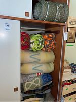 View of folded wool blankets and rolled quilted sleeping bags in a wooden wardrobe shelving