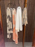 Four blankets and one curtain hanging on metal hangers against wood paneling.