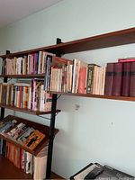 Five shelves holding a variety of books in paperback and hardcover with titles in English and Dutch.