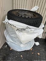 Four tires on steel rims stacked wrapped in plastic bags in a shed area.