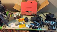 Photo showing cameras, Kodak pocket guide, Sony Discman box, camera cases and cables.