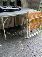 Photo showing Broadstone camp table with foldable metal legs and lawn chair with patterned woven fabric seat behind it.