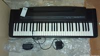 Full view of Roland EP-5 digital piano keyboard placed on a clear plastic sheet on concrete floor with foot pedal and power adapter cables visible.