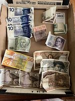 And overview photo showing multiple foreign currency bills laid flat and some folded, including French Francs, Deutsche Mark, and Dutch Gulden.