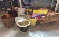 Photo of assorted gardening pots, gloves, lawn bags packaging, and a wooden basket on basement floor
