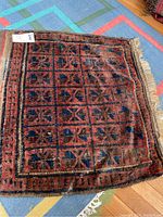 Full view of square hand woven rug showing geometric red, brown, blue pattern and fringe.